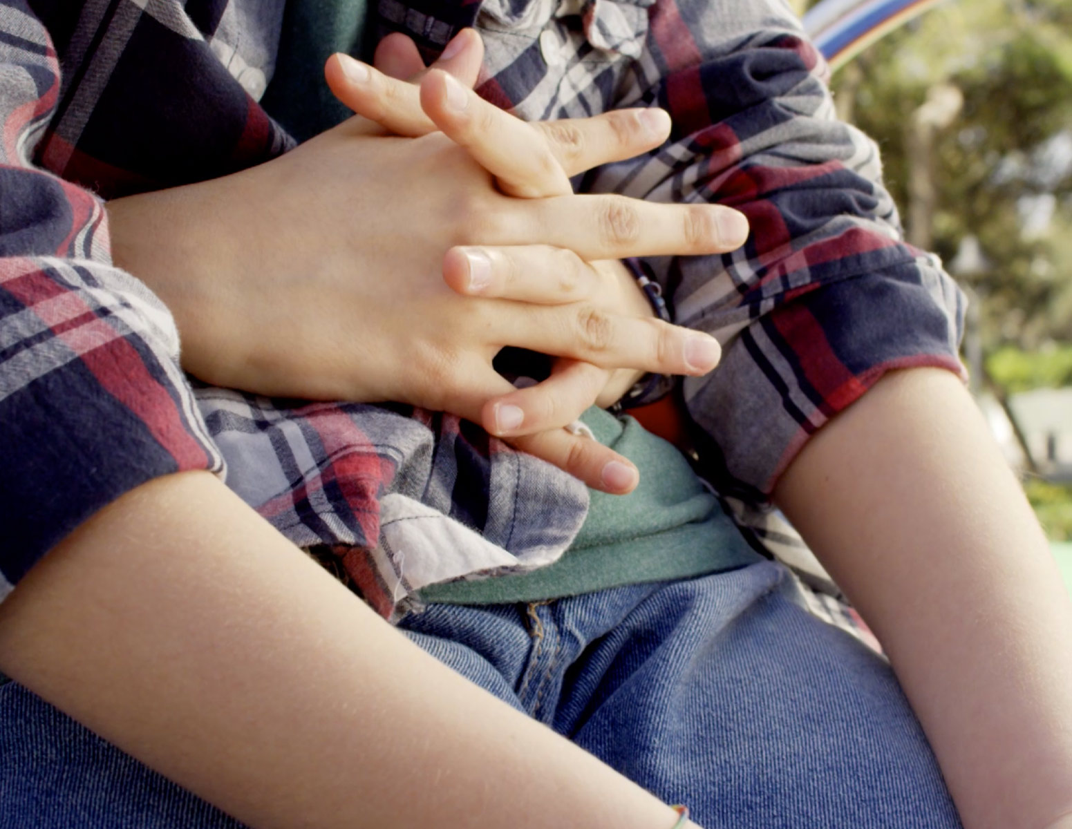 Foto del dettaglio di due mani che abbracciano da dietro un bambino.
